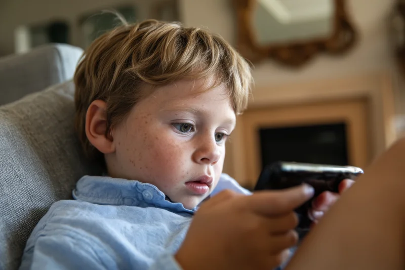 Young boy concentrating on smartphone while reclining on sofa in living room