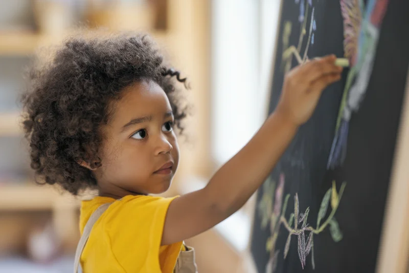 Young child drawing with chalk on a blackboard in a classroom setting