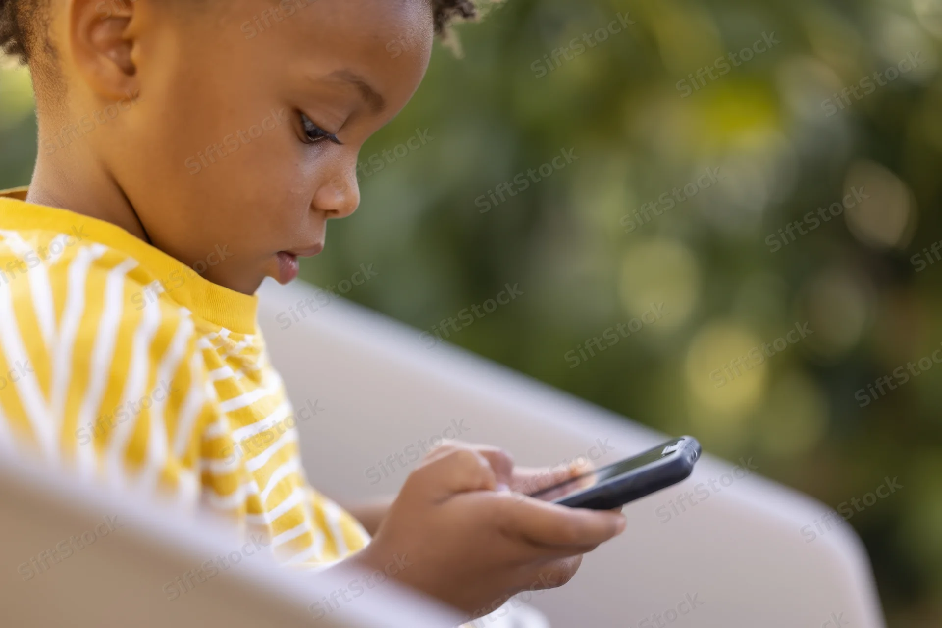 Young child focused on smartphone screen outdoors holding device with both hands