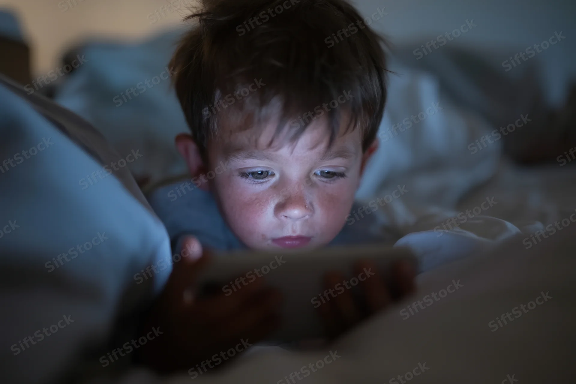 Young boy lying in bed focused on smartphone screen at night