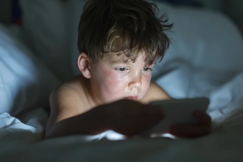 Young boy lying in bed concentrating on a smartphone screen at night