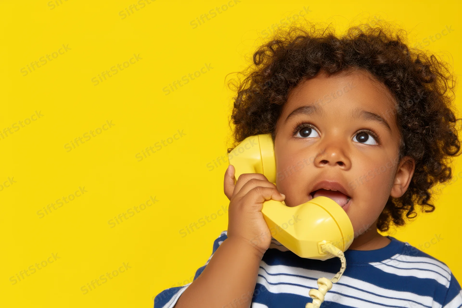 Young child with curly hair holding vintage yellow rotary phone against bright yellow background