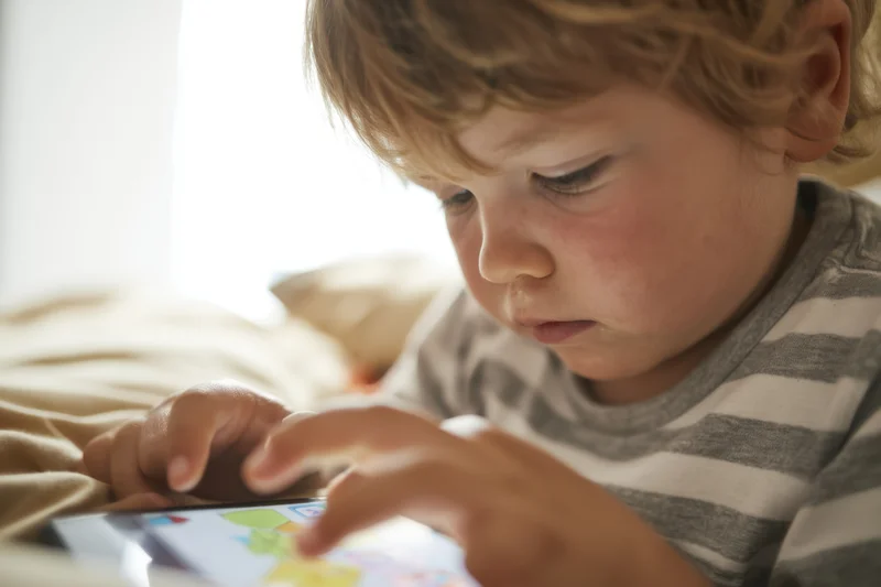 Young boy concentrating on a tablet while lying on a bed at home