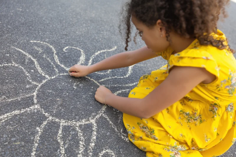 Young girl drawing a sun with chalk on textured asphalt pavement