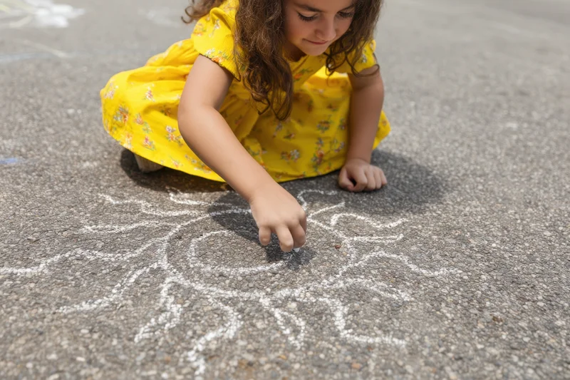Young girl drawing with chalk on textured asphalt pavement outdoors