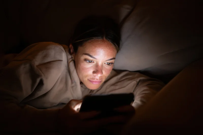 Woman lying on couch illuminated by smartphone screen light at night