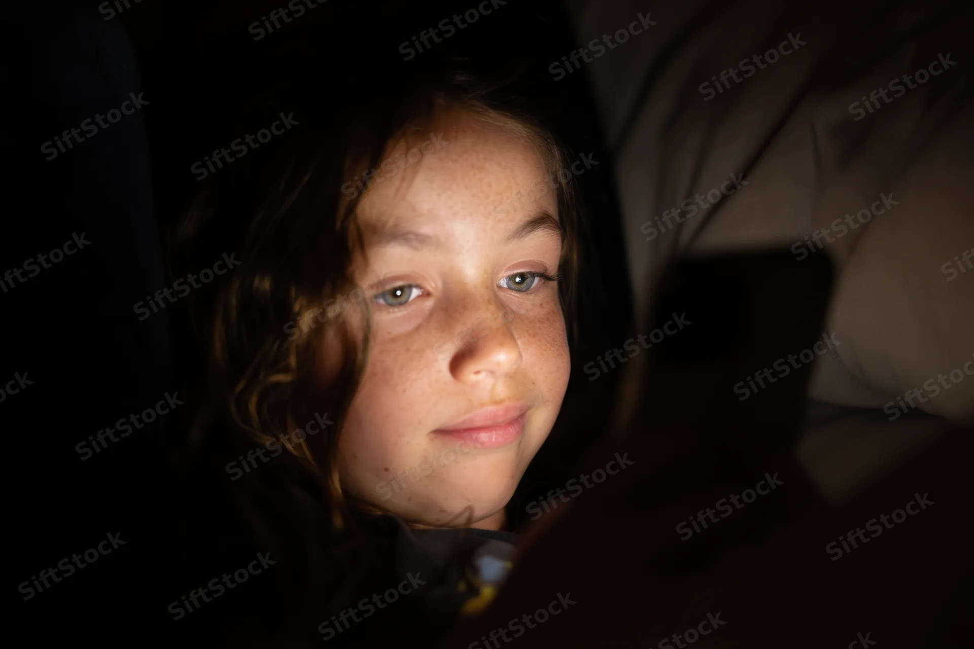 Young girl lying on couch illuminated by smartphone screen light at night