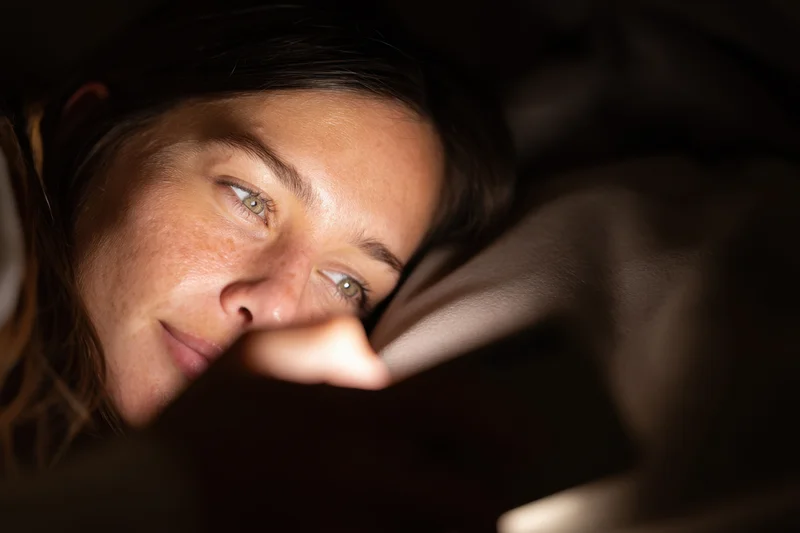 Woman lying in bed illuminated by smartphone screen light at night