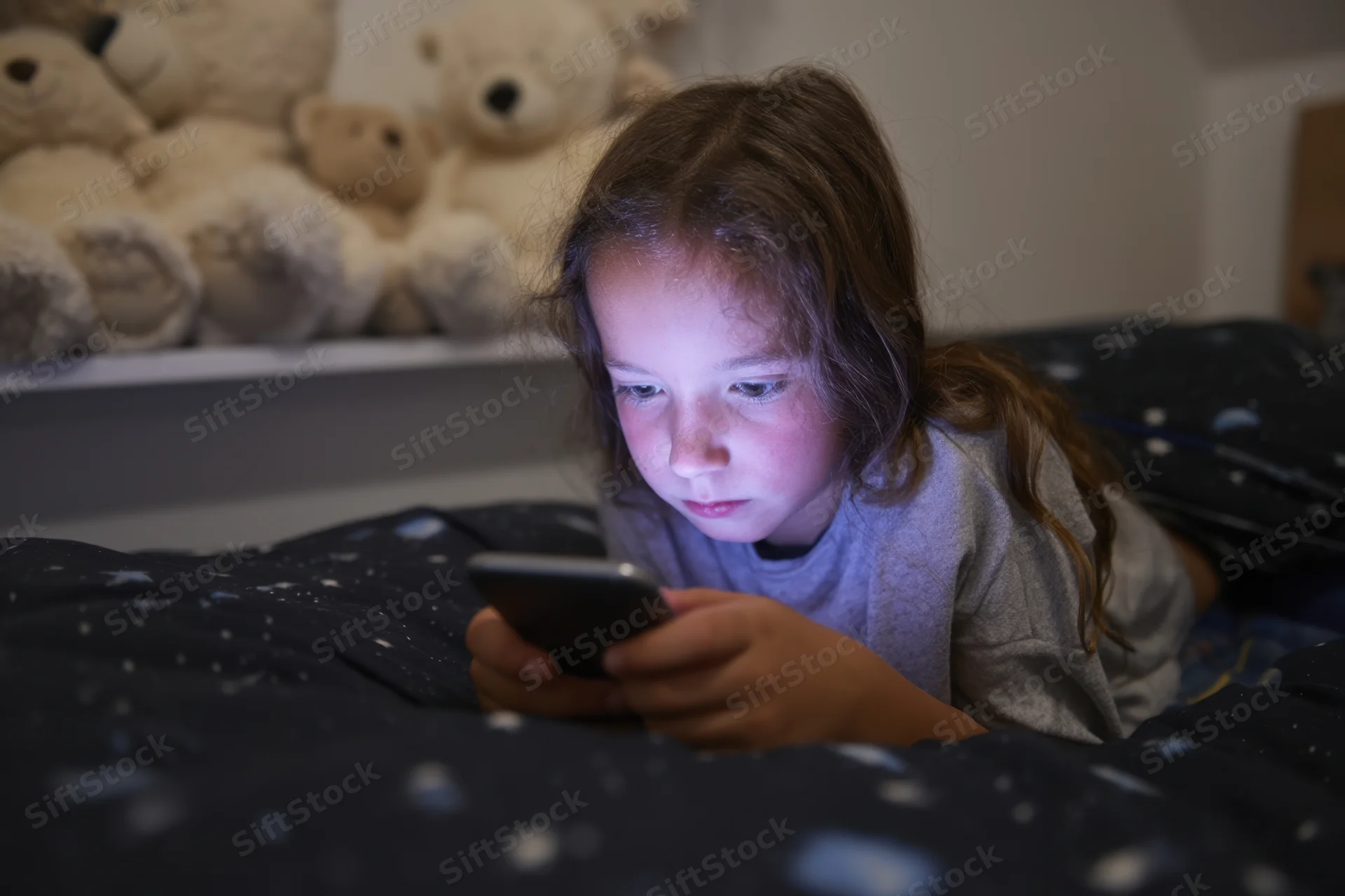 Young girl lying in bed focused on her smartphone at night