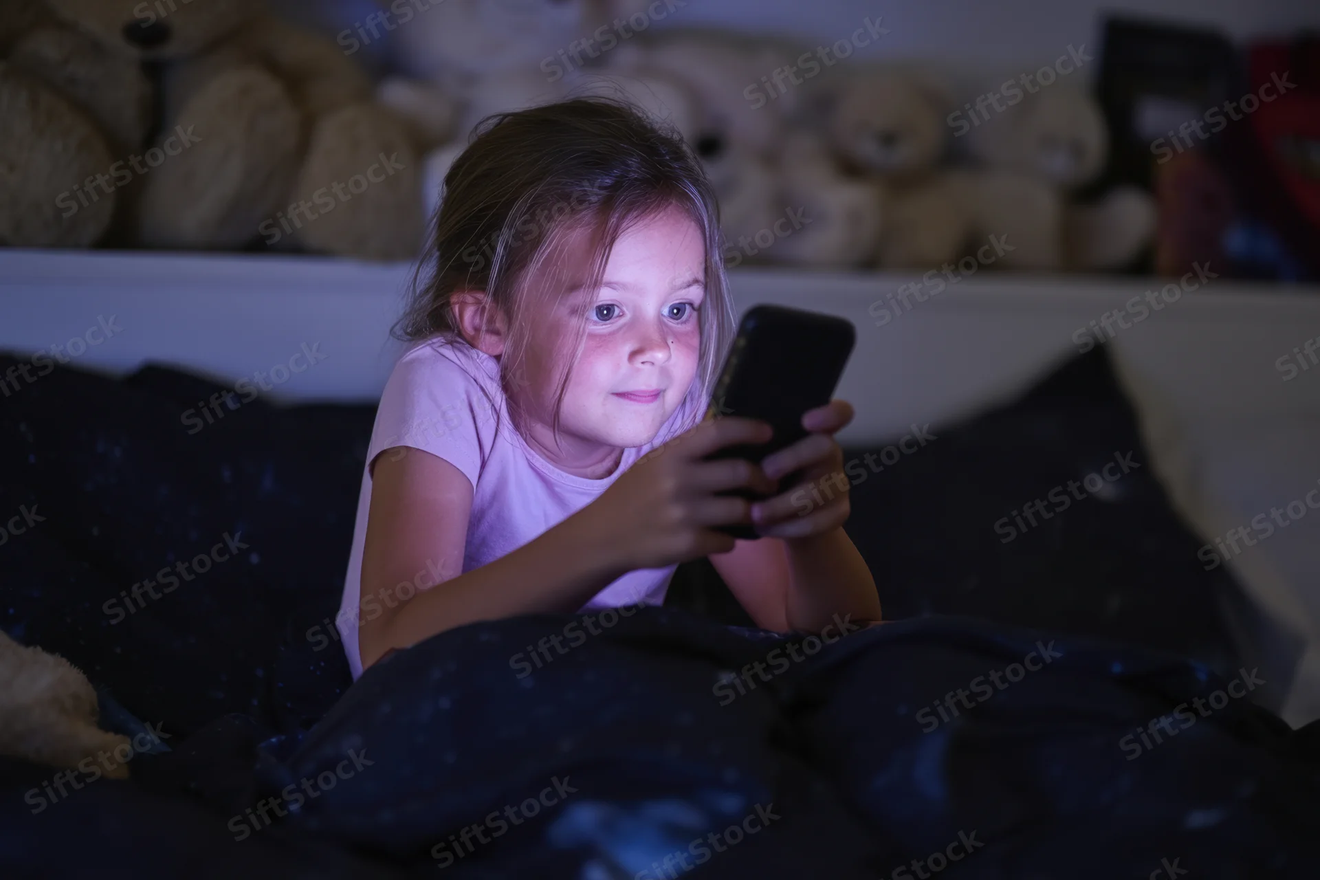 Young girl lying in bed focused on smartphone screen at night