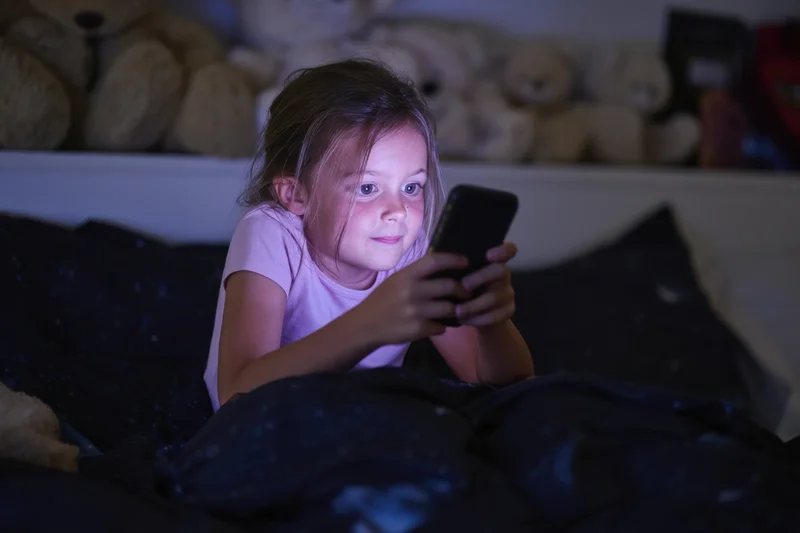 Young girl lying in bed focused on smartphone screen at night