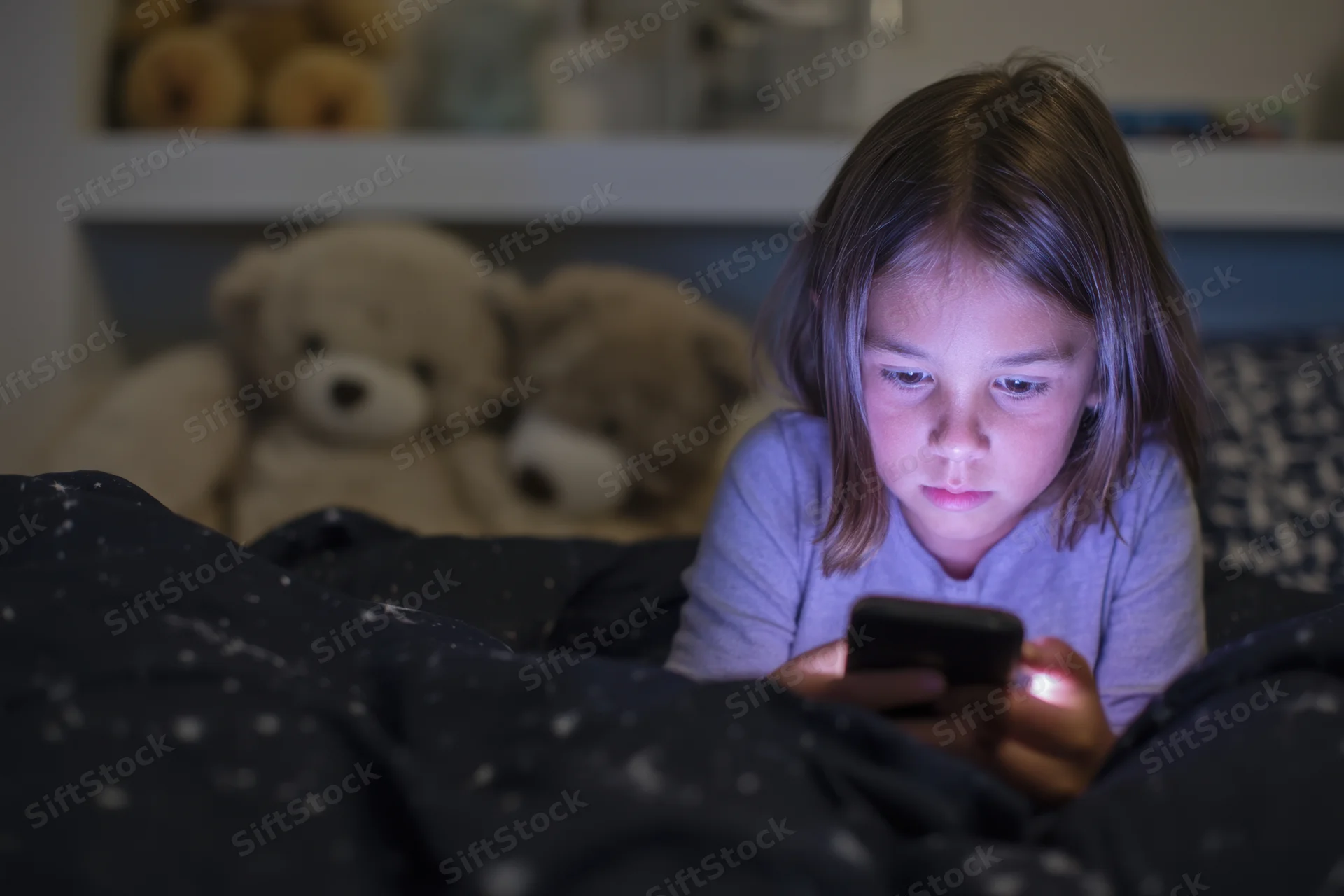 Young girl lying in bed focused on smartphone screen at night