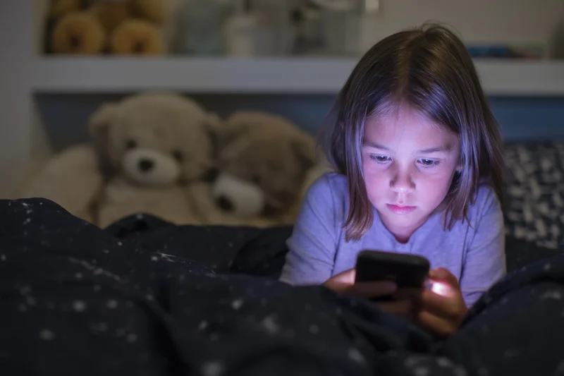 Young girl lying in bed focused on smartphone screen at night