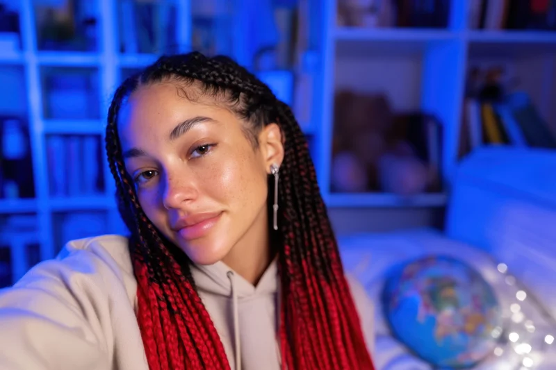 Young woman taking a selfie in a cozy bedroom with blue lighting and string lights