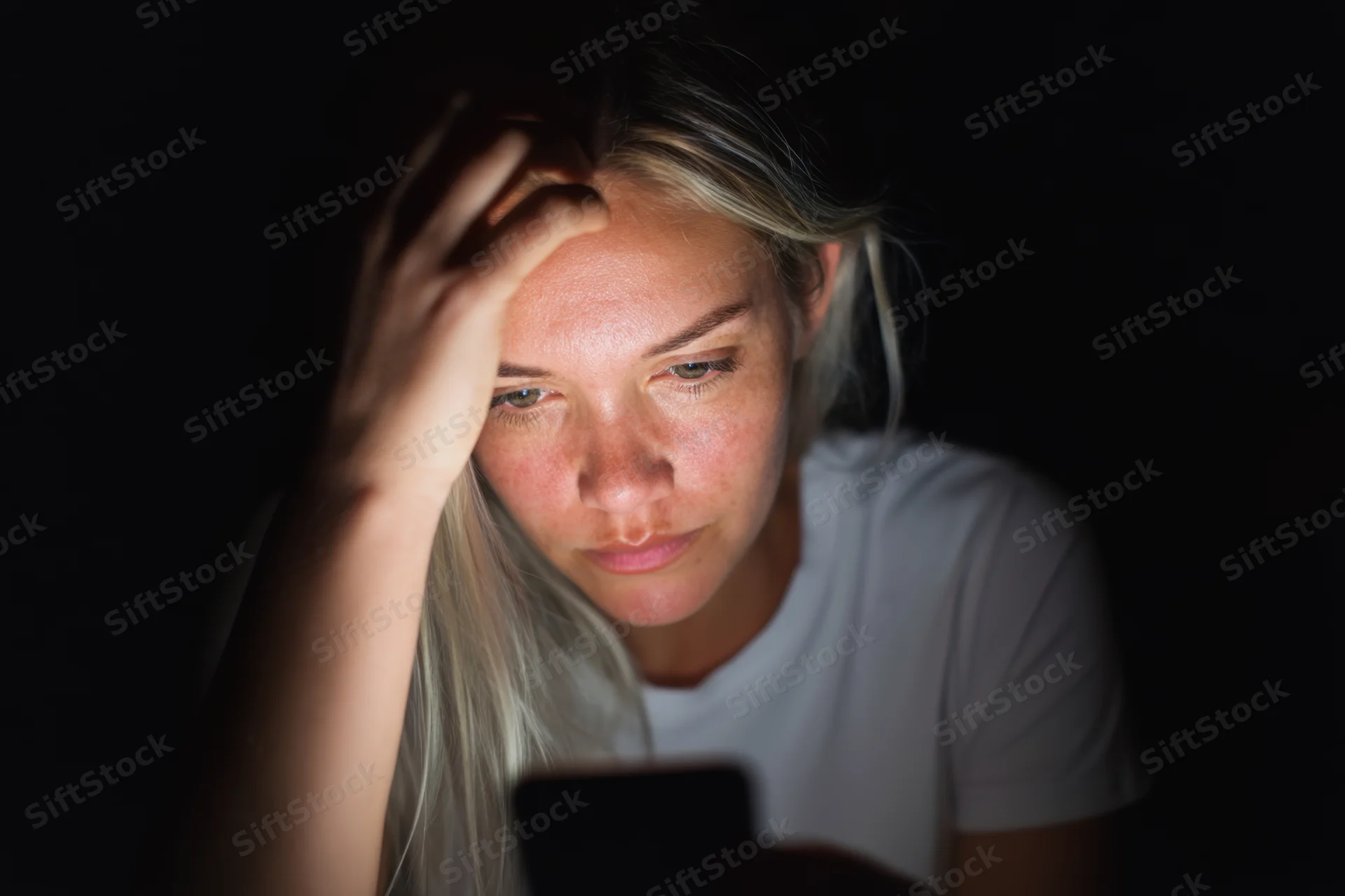 Young woman focused on smartphone screen in dark room at night