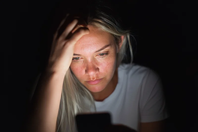 Young woman focused on smartphone screen in dark room at night