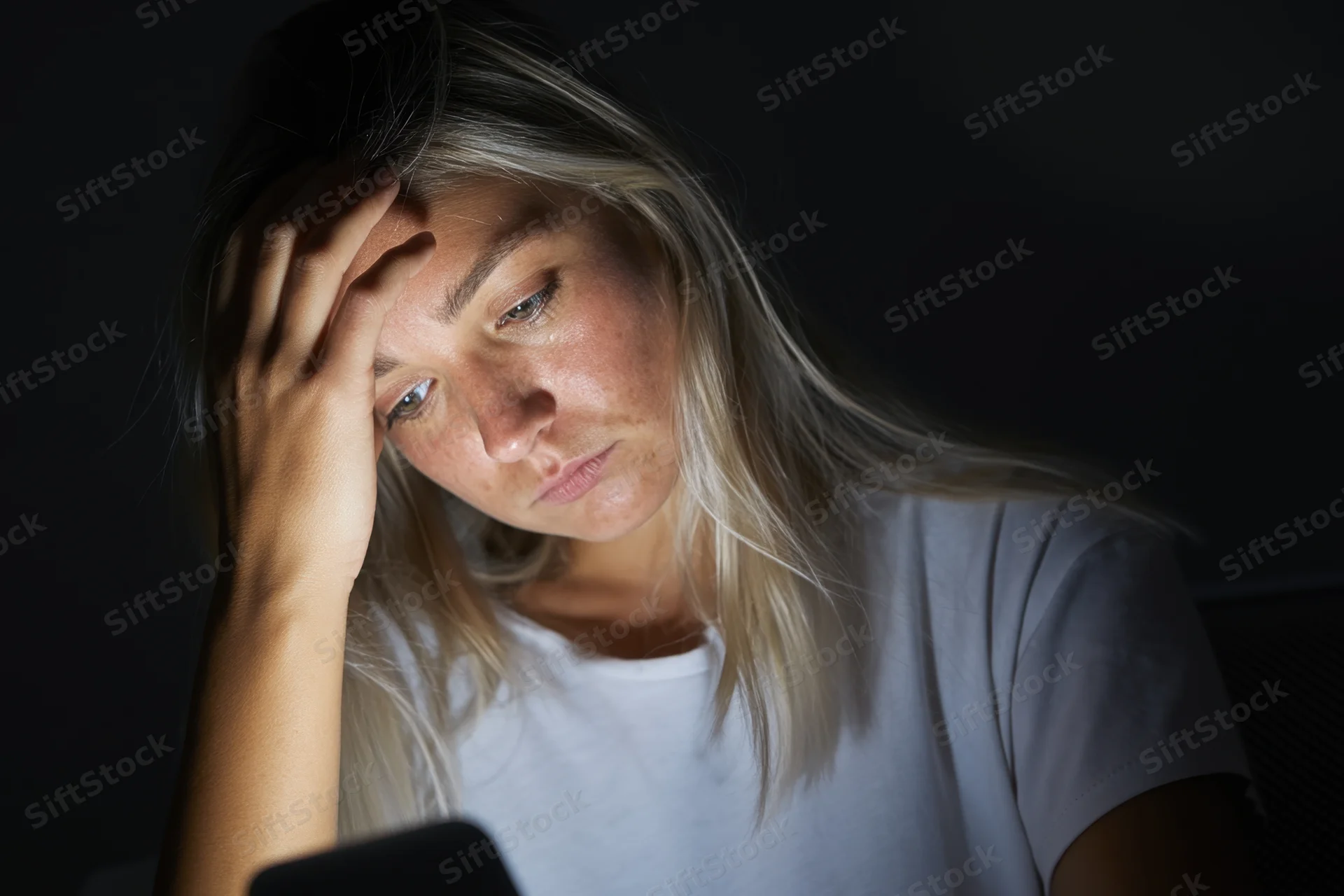 Of a young woman in a dark room illuminated by the screen