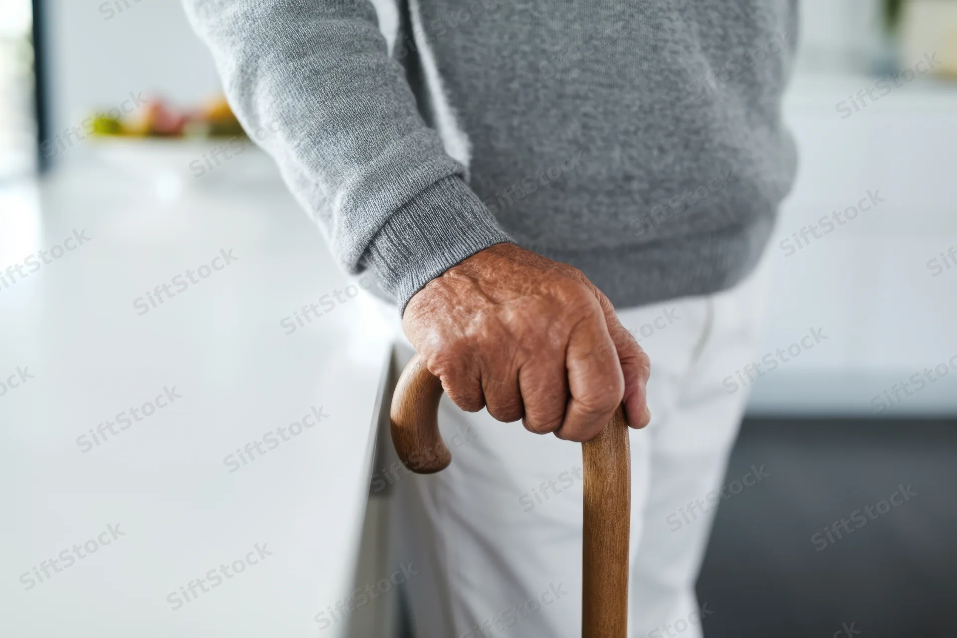 Senior man holding wooden cane while standing in modern kitchen interior