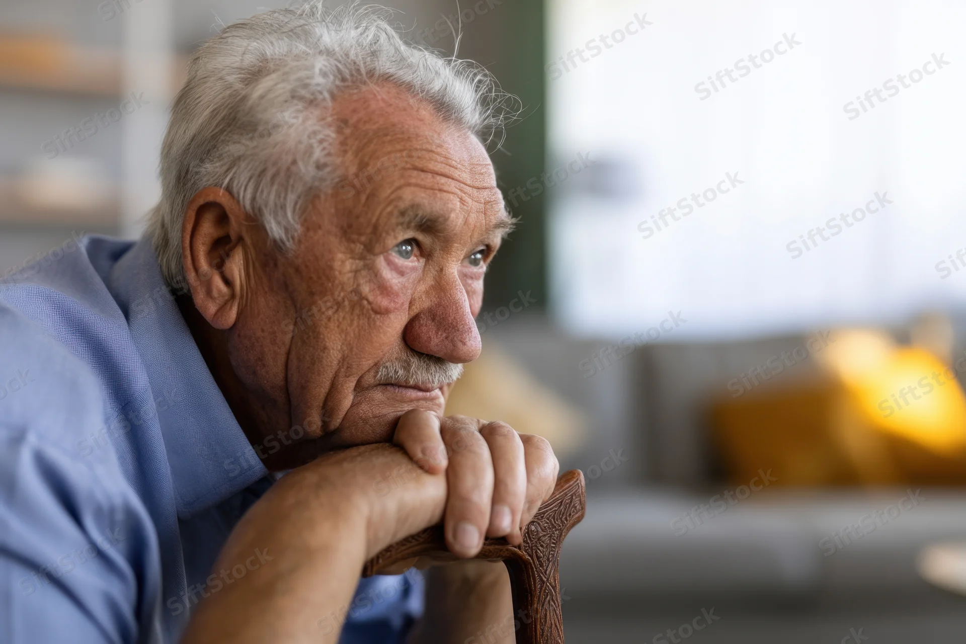 Elderly man resting his chin on hands gripping a carved wooden cane indoors