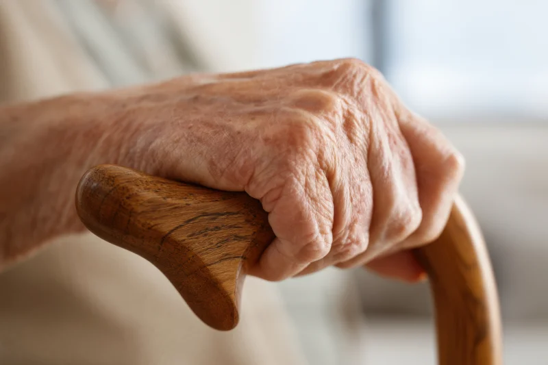 Elderly woman's hand gripping a wooden cane indoors