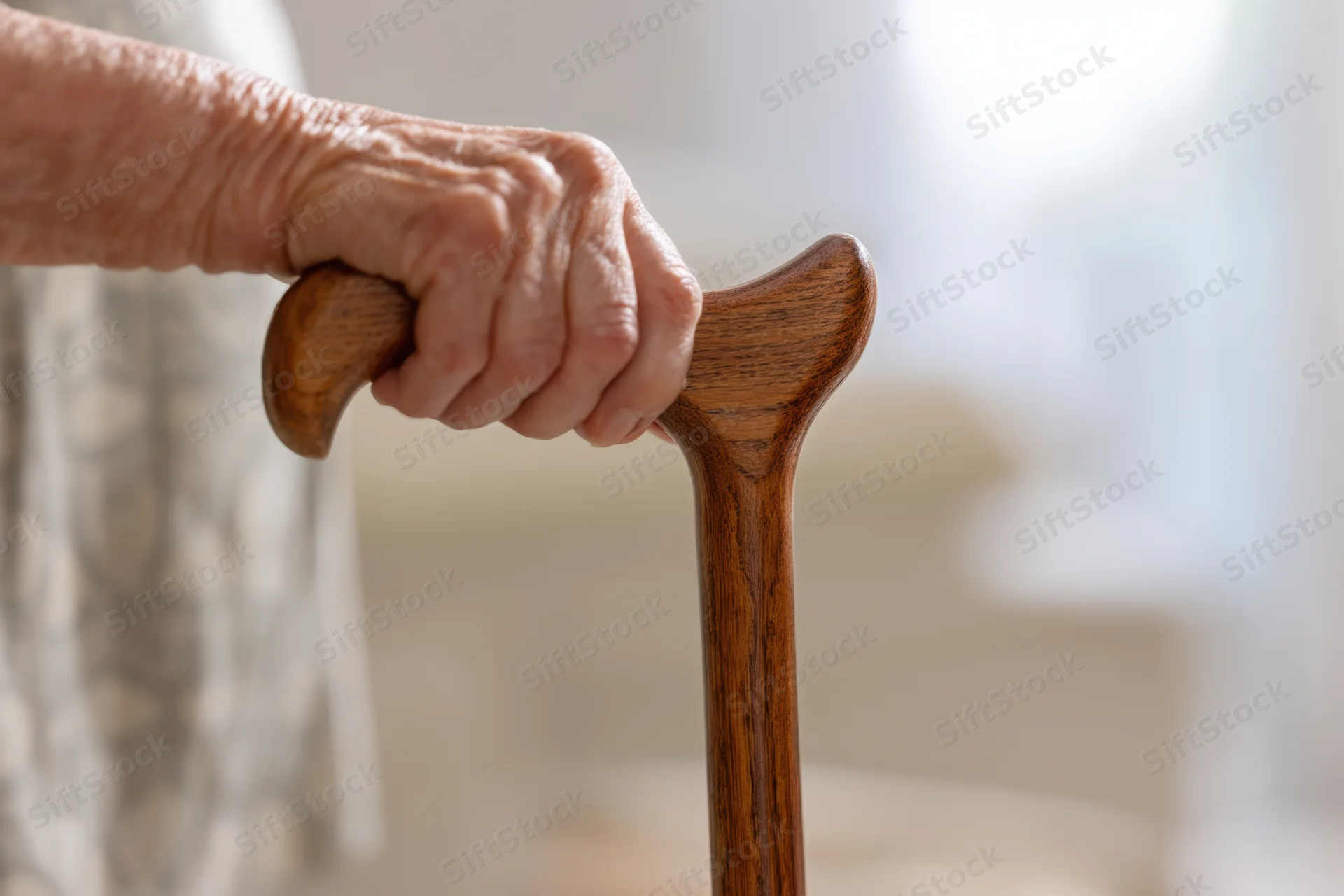 Elderly woman's hand gripping a wooden cane indoors