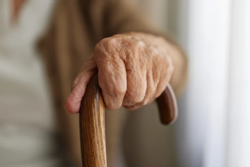 Elderly woman's hand gripping a wooden cane indoors