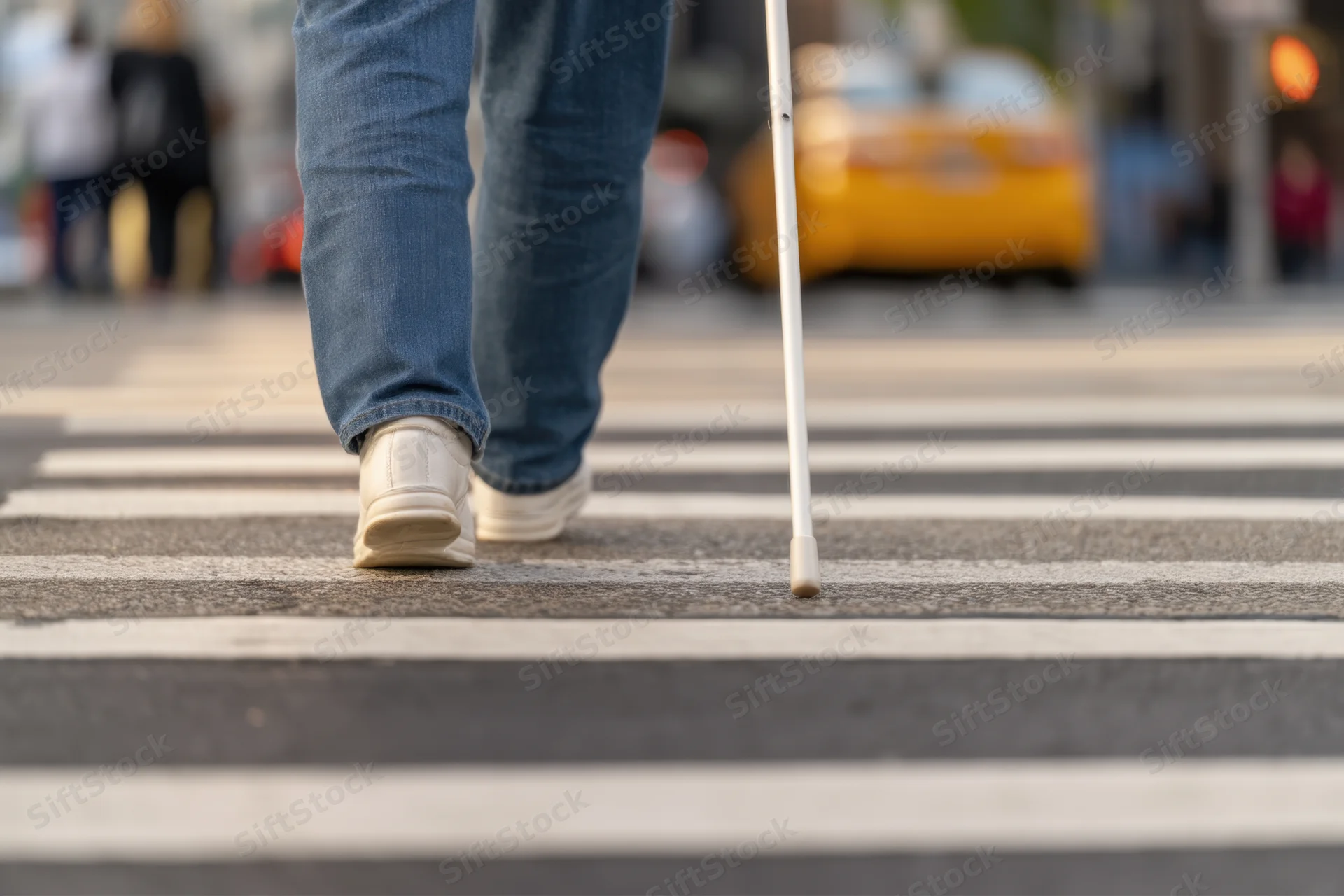 Person walking with white cane across city crosswalk