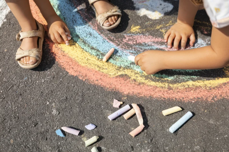Children’s hands drawing with colorful chalk on asphalt pavement