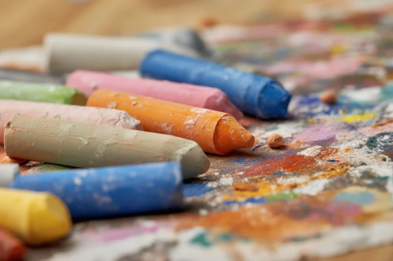 Colorful art pastels arranged on a textured surface with scattered pigment and dust