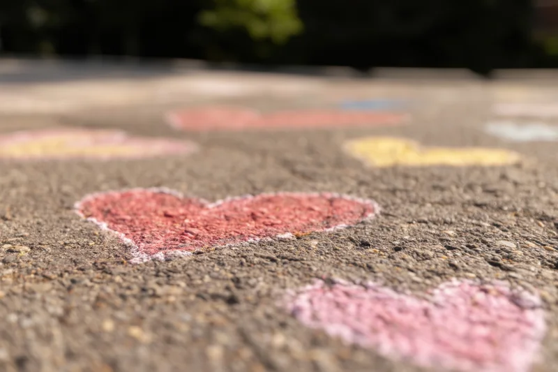Colorful heart shapes drawn with chalk on textured asphalt pavement