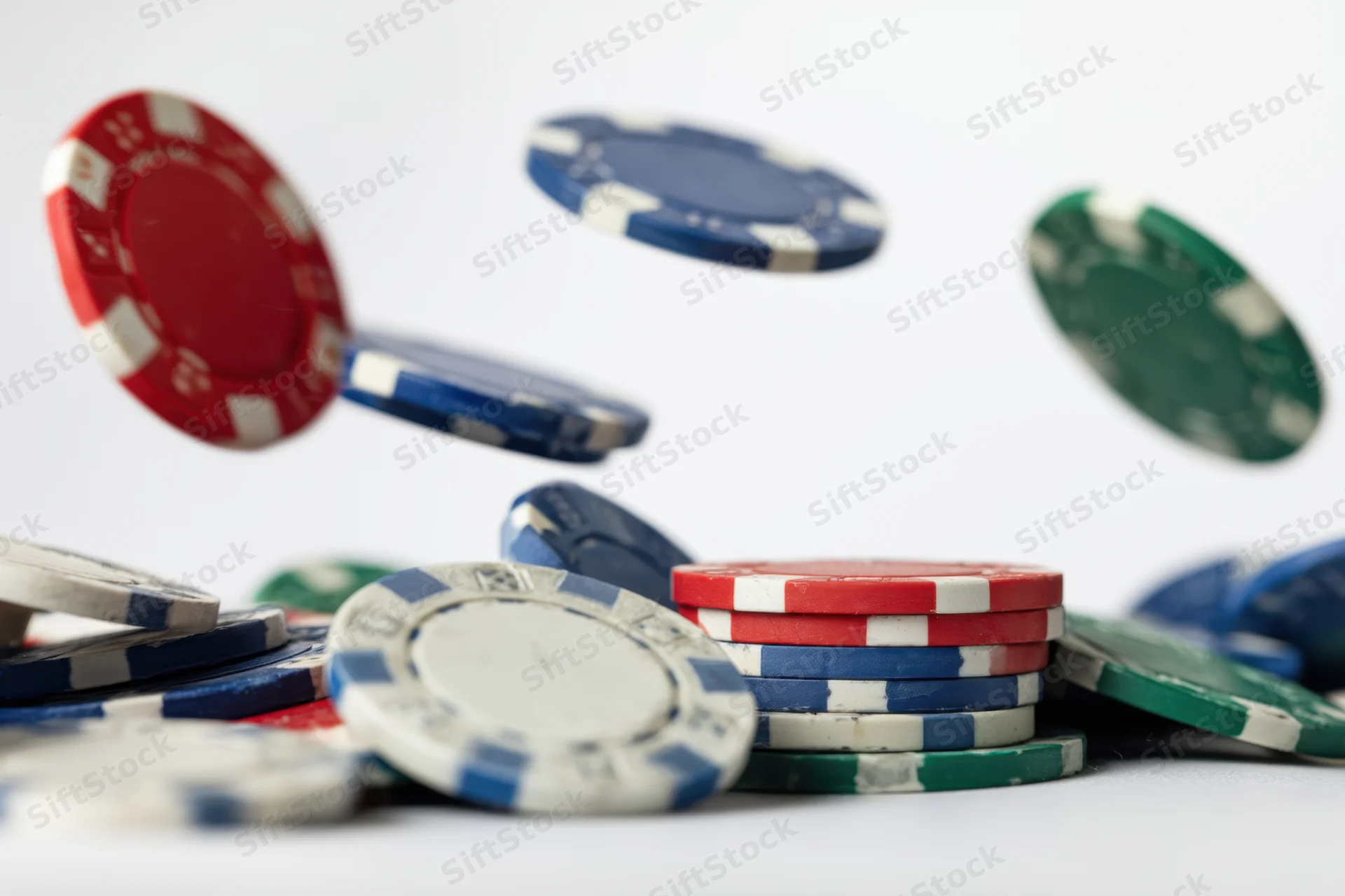 Falling poker chips in red blue green and white mid-air above a pile on white surface