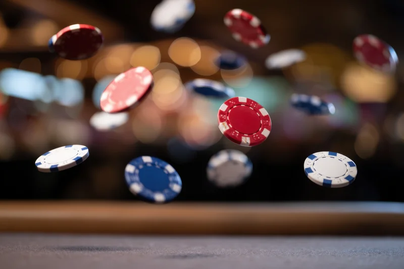 Poker chips falling in midair over a casino table with blurred bokeh lights in the background