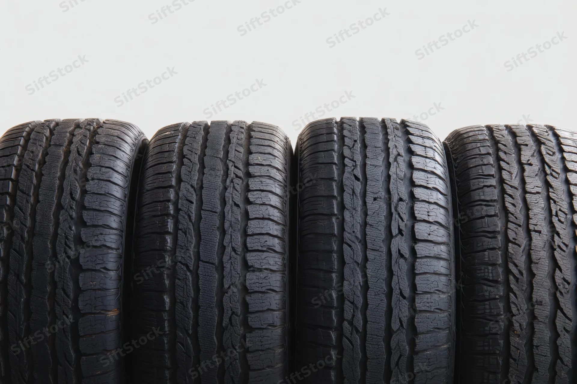 Four black automotive tires arranged side by side showing worn tread patterns against a plain background