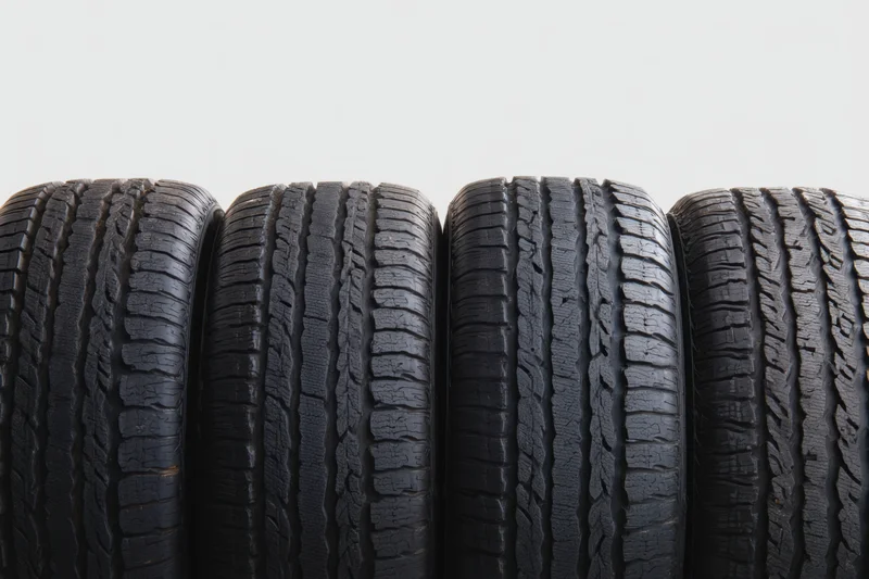 Four black automotive tires arranged side by side showing worn tread patterns against a plain background