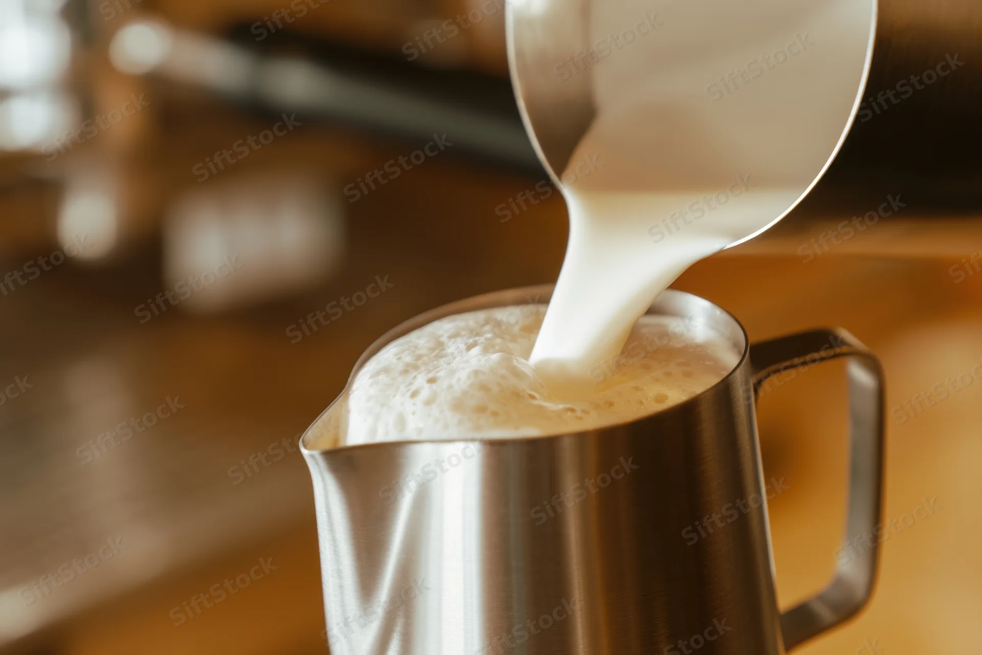 Steamed milk pouring into a stainless steel pitcher on a wooden counter
