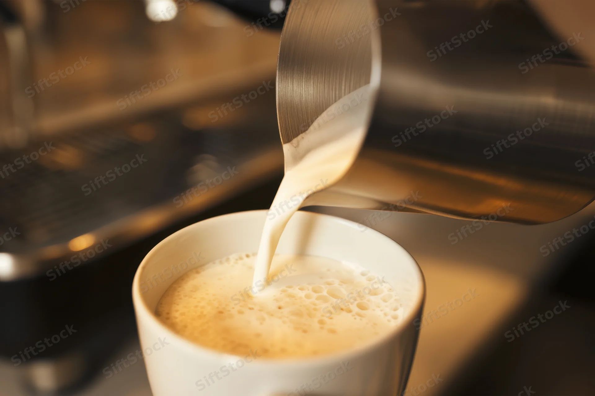 Steamed milk pouring into a white ceramic cup with froth, in a coffee shop setting