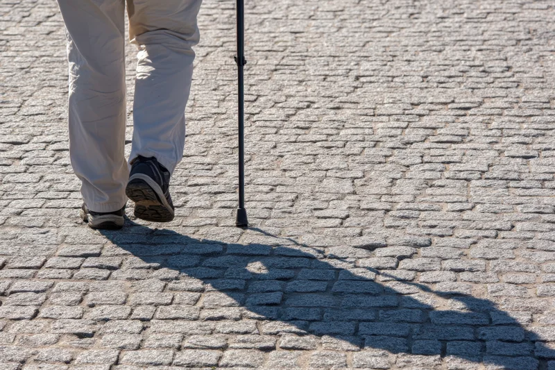 Senior person walking with cane on cobblestone pavement