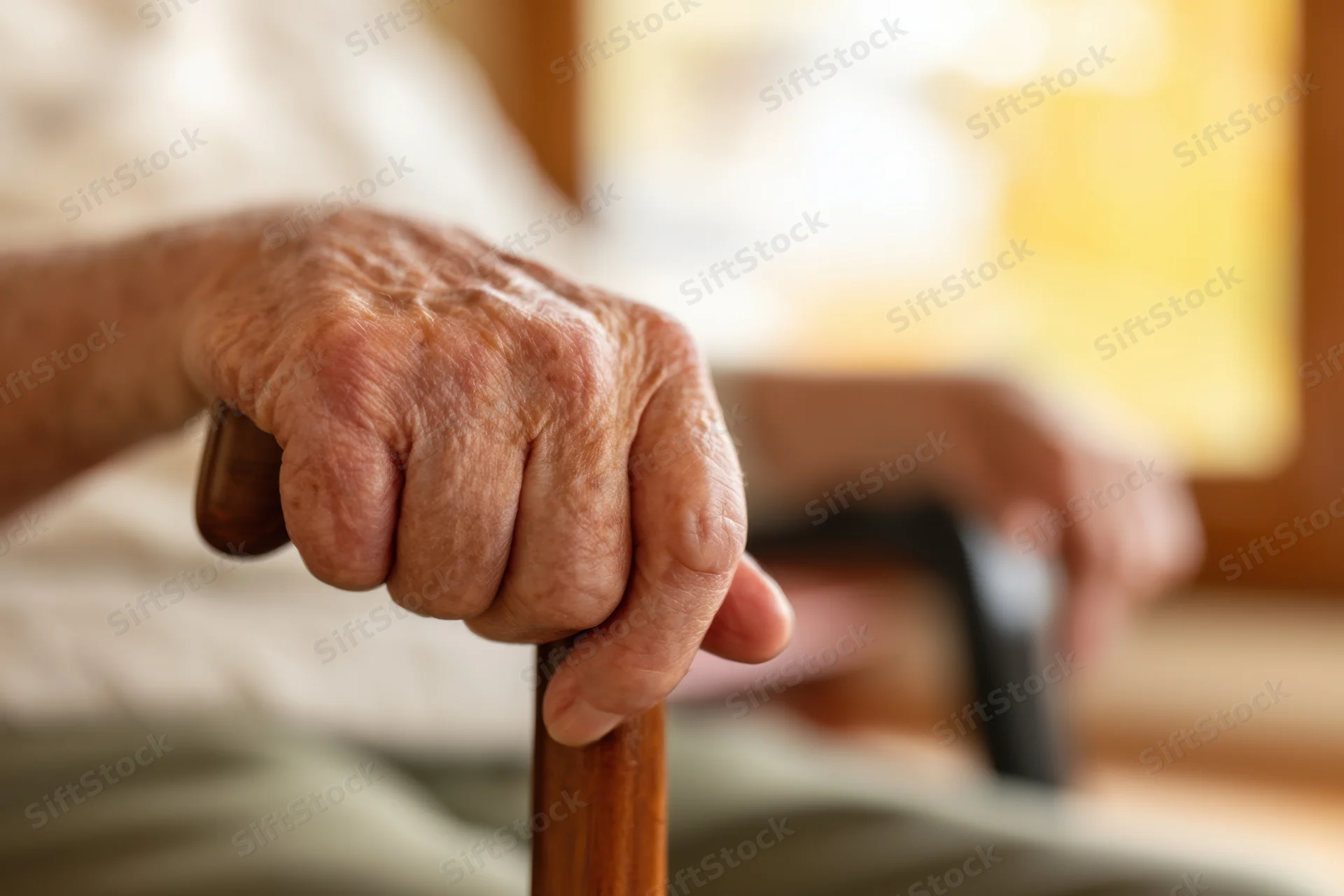 Senior hand gripping a wooden cane for support indoors