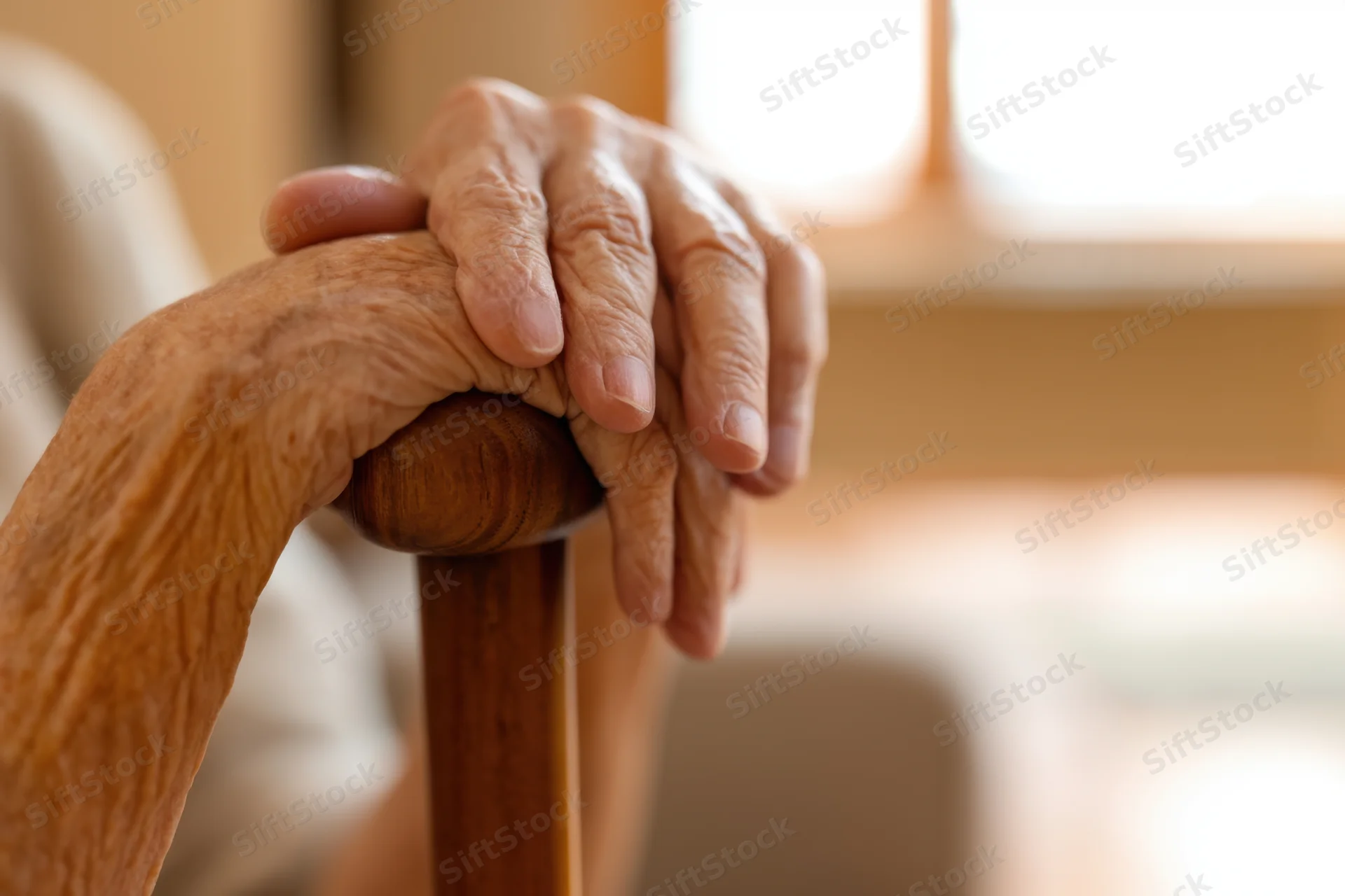Elderly hands resting on a wooden cane indoors