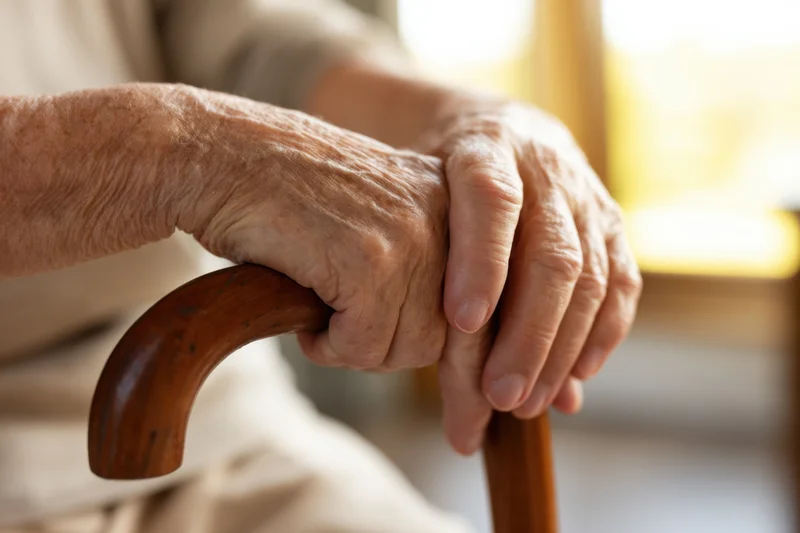 Elderly hands resting on a wooden cane indoors