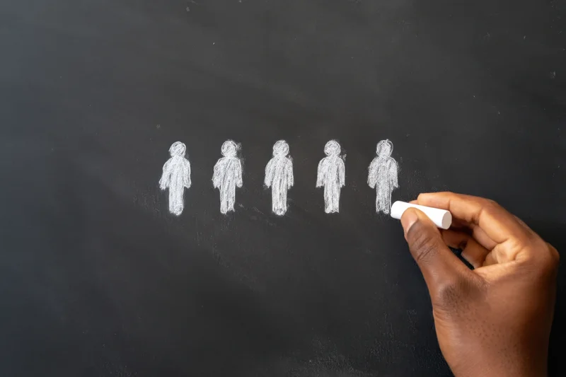 Hand drawing five simple human figures in a row on a chalkboard with white chalk