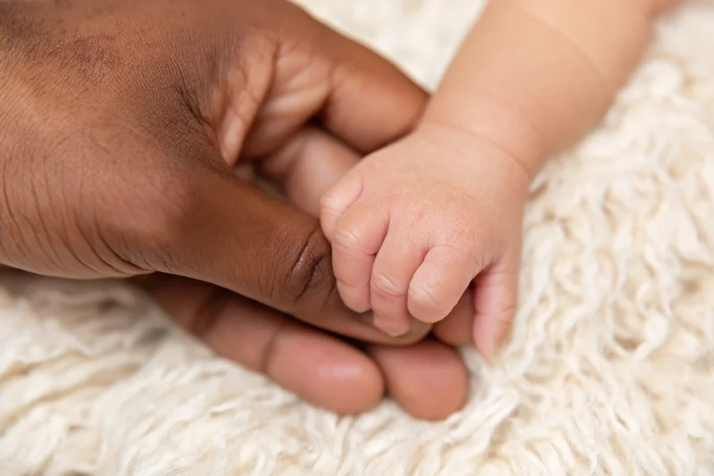 Adult hand gently holding baby's hand on a soft white blanket