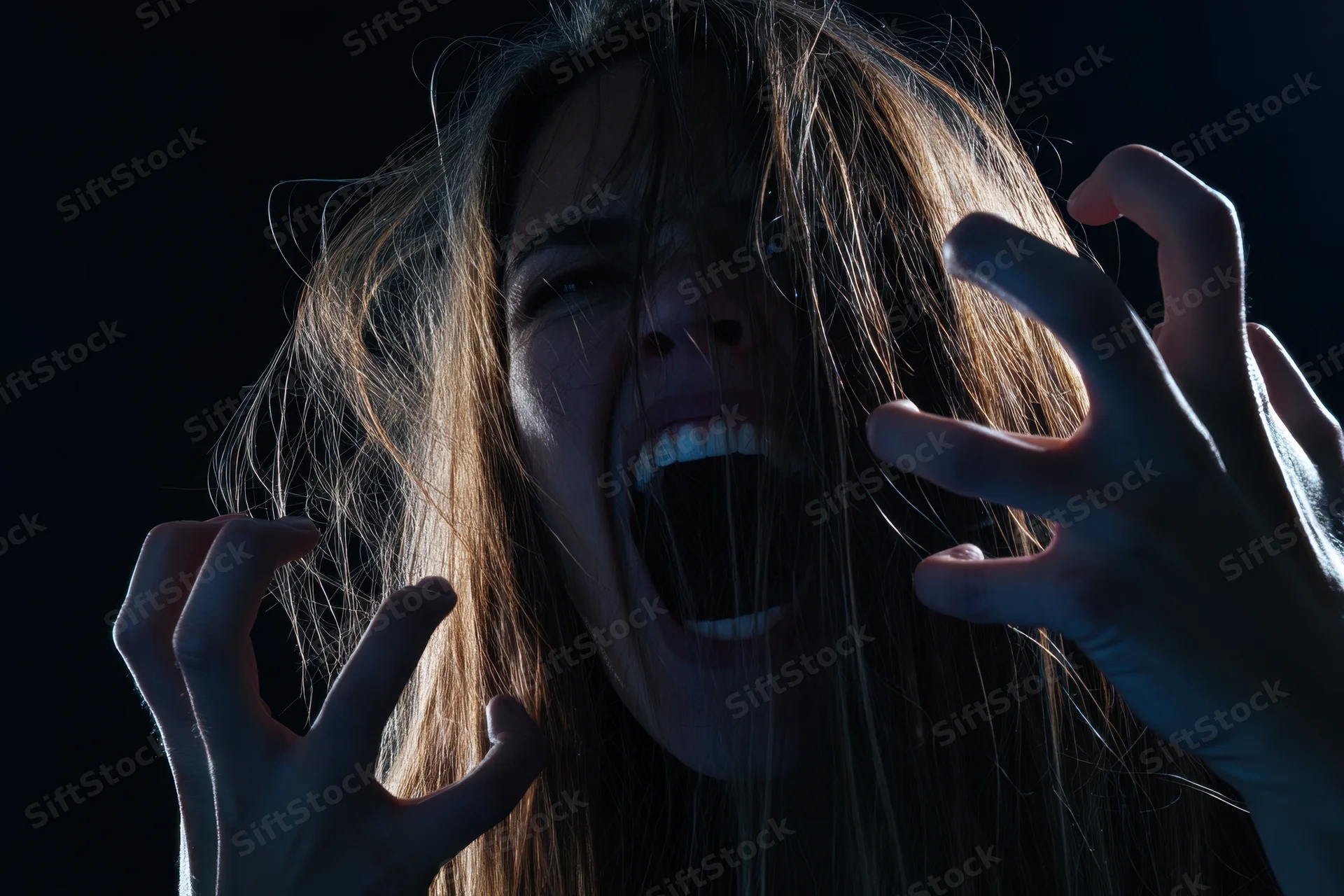 Woman screaming with long messy hair and hands raised in dark dramatic lighting