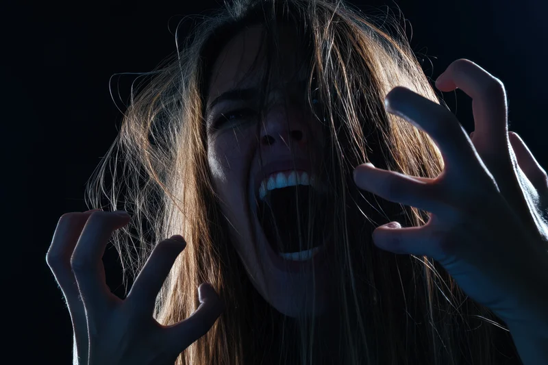 Woman screaming with long messy hair and hands raised in dark dramatic lighting