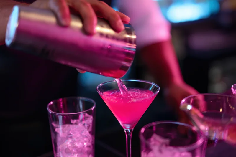 Bartender pouring pink cocktail into martini glass at bar