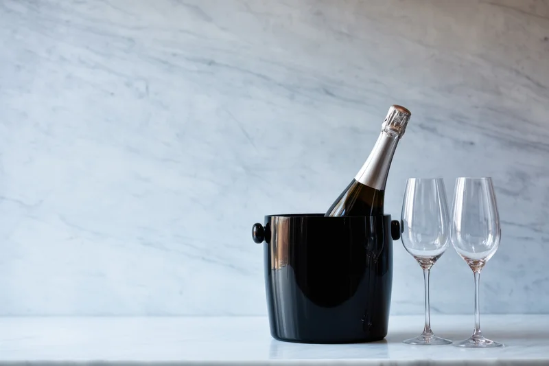Champagne bottle in black bucket with two flutes on marble countertop
