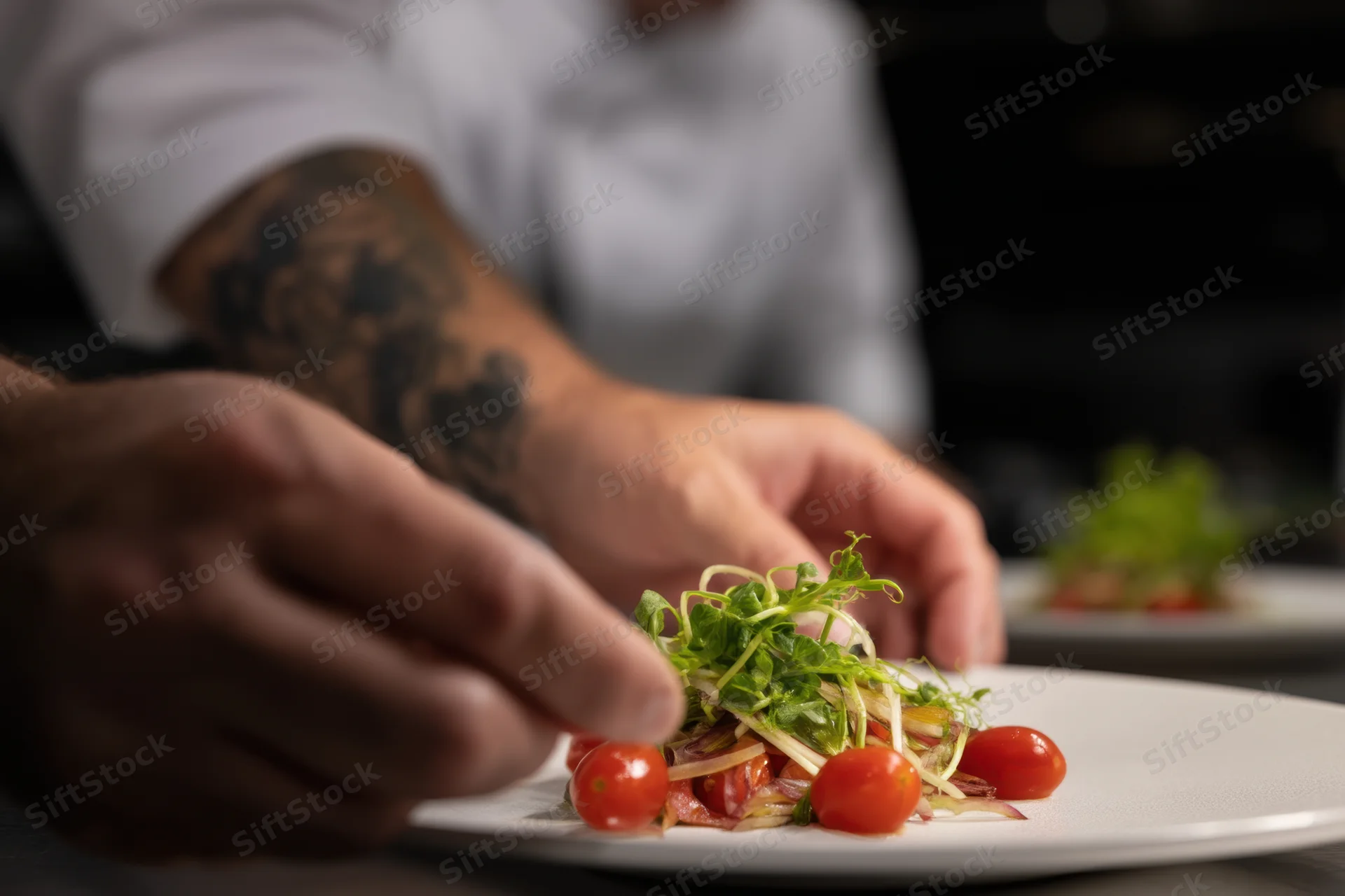 Chef's hands plating a gourmet dish with cherry tomatoes and microgreens on a white plate