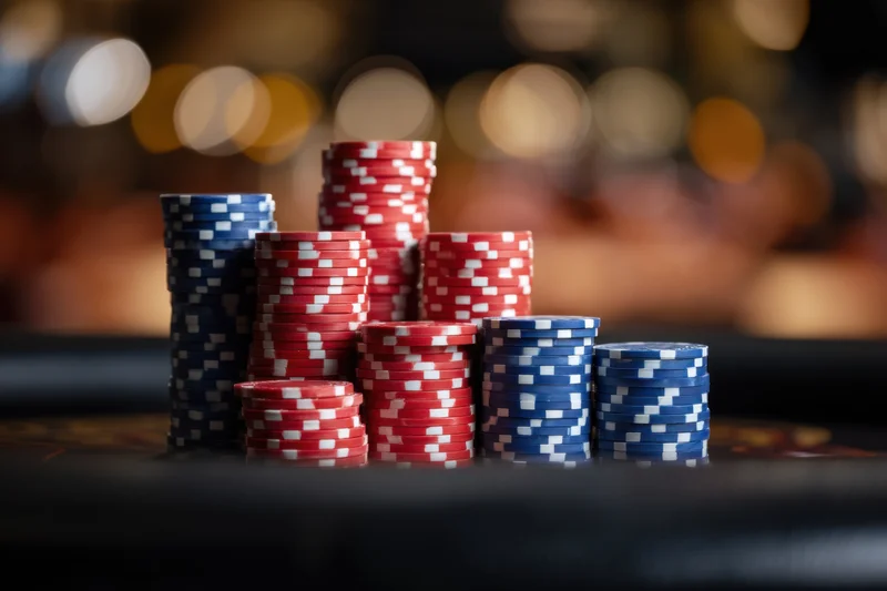 Stacks of red and blue poker chips arranged on a casino table with blurred lights in the background