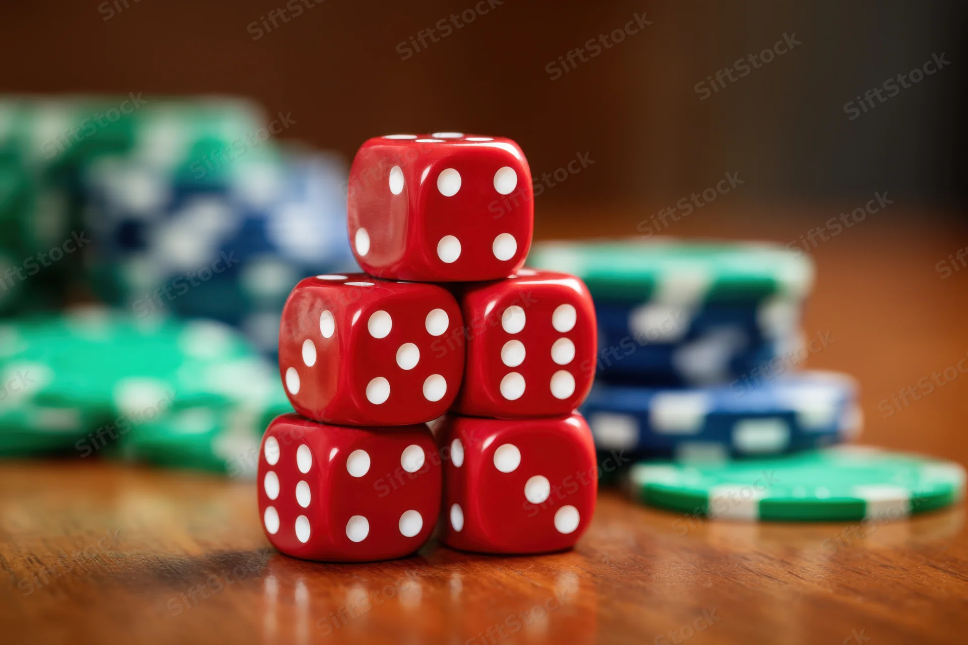Five red dice stacked in a pyramid on a wooden table with poker chips in the background