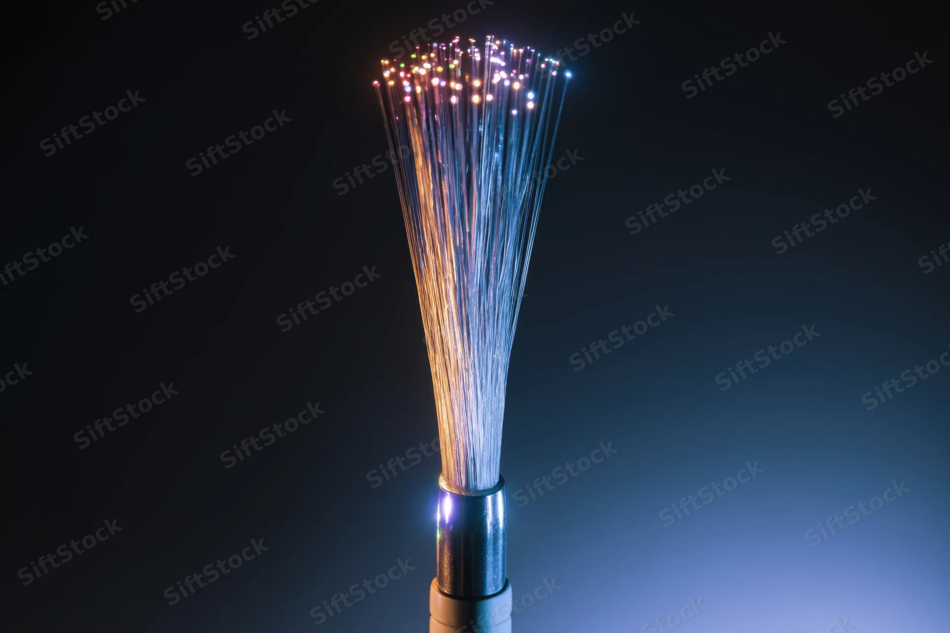 Close-up of fiber optic cable with glowing multicolored strands fanning out from connector against dark background